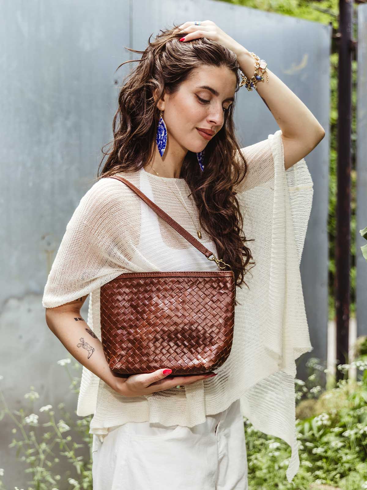 Close-up of a woman carrying a handwoven brown leather crossbody bag, highlighting the intricate woven leather design and strap.