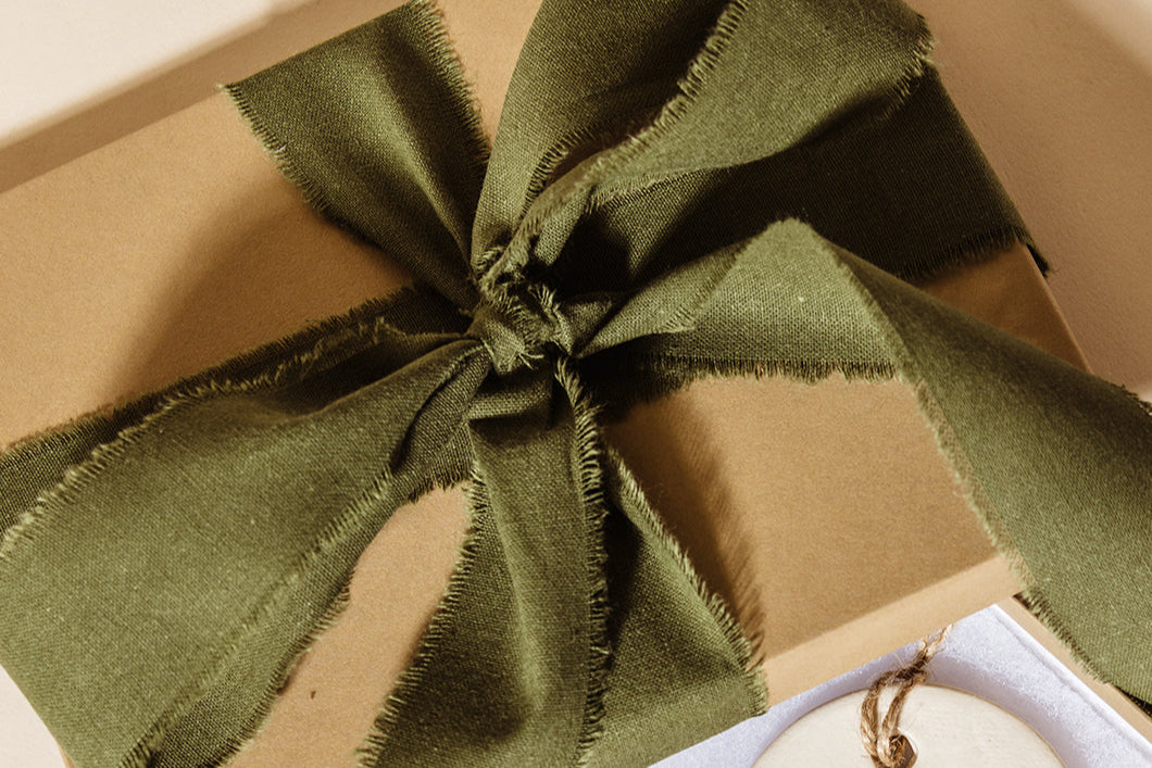 Gift box opened to reveal ceramic “Hope,” “Peace,” and “Joy” ornaments nestled inside, accented with a frayed green ribbon for a heartfelt and meaningful holiday gifting presentation.